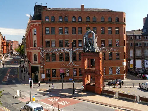 Tall red brick building with decorative arch and sculpture, under blue sky on sunny day. Cars drive below.