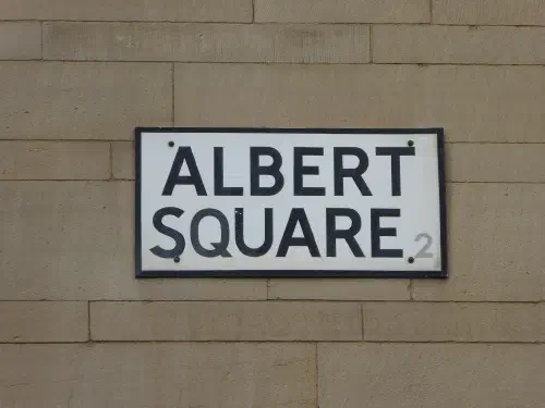 A white street sign on a tan stone wall reads "ALBERT SQUARE" with number 2.