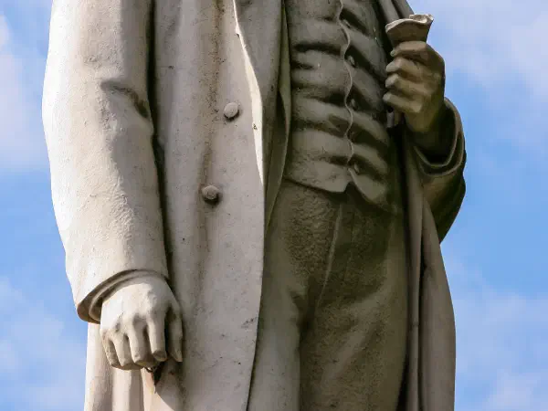 Statue against blue sky; one face visible, other obscured by shadow. — Albert Square, Manchester