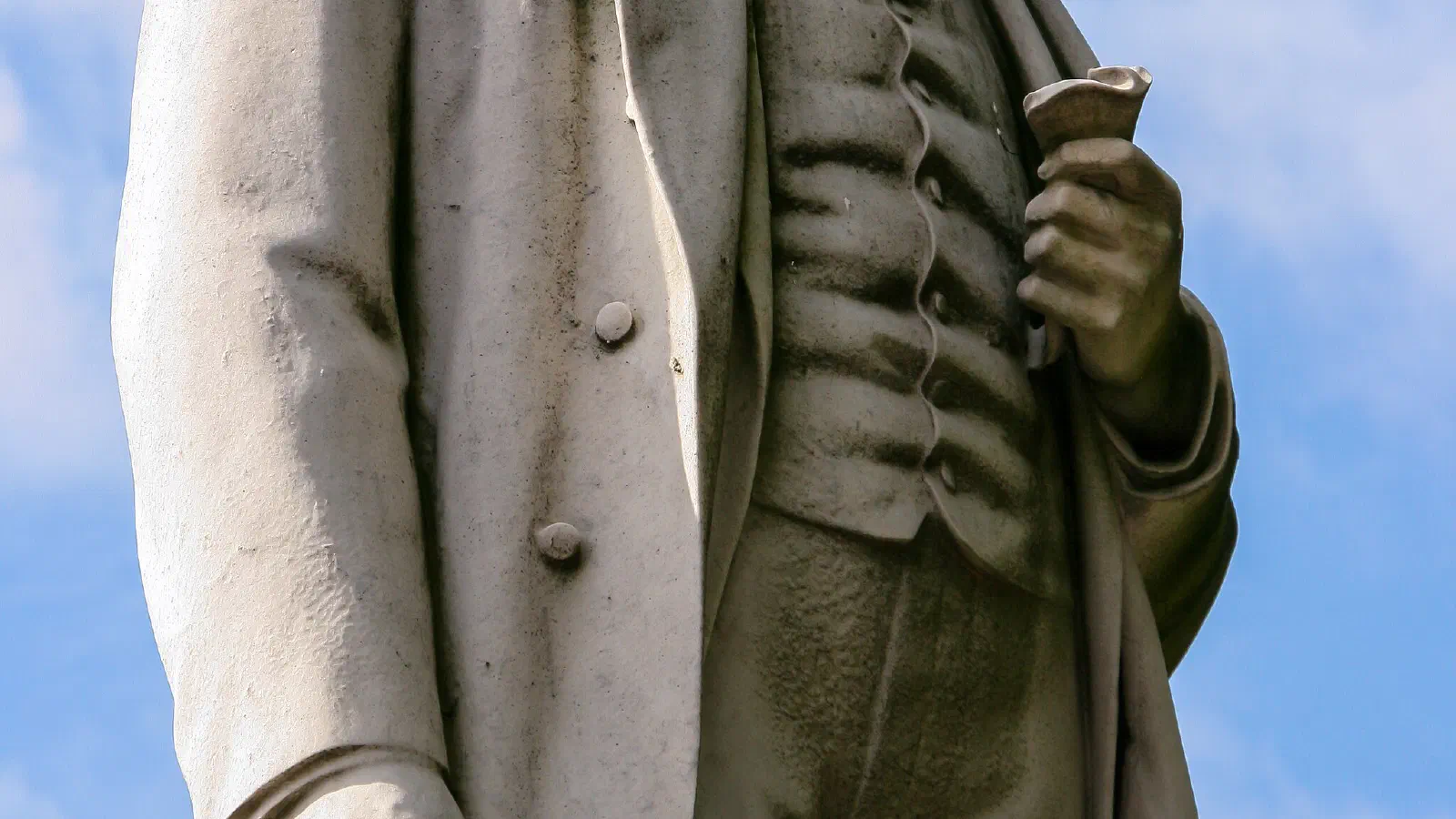 Statue against blue sky; one face visible, other obscured by shadow. — Albert Square, Manchester
