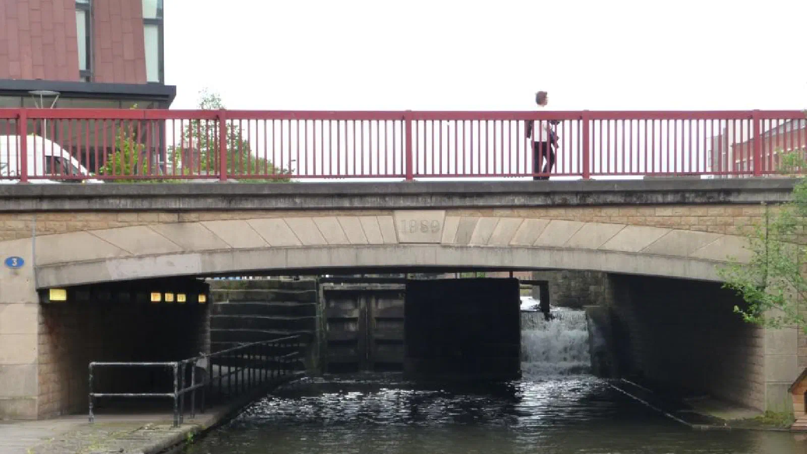 Stone bridge spans canal below lock gate under red railing and sky above. — Ancoats Bridge (Ashton Canal), Manchester