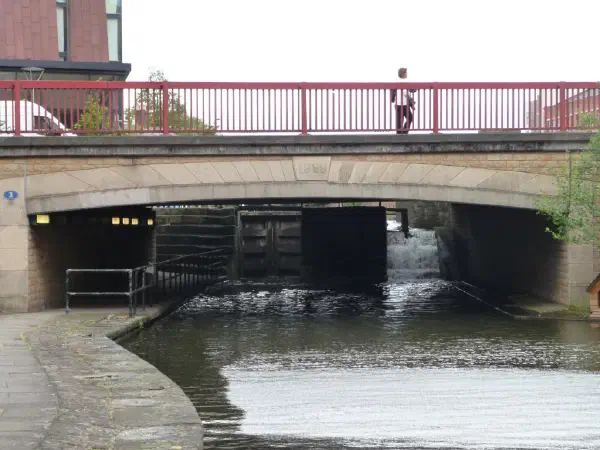 Stone bridge spans canal below lock gate under red railing and sky above. — Ancoats Bridge (Ashton Canal), Manchester