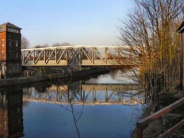 A canal bridge reflecting on calm water beside a brick structure under clear sky. — Barton Swing Bridge & Aqueduct, Manchester