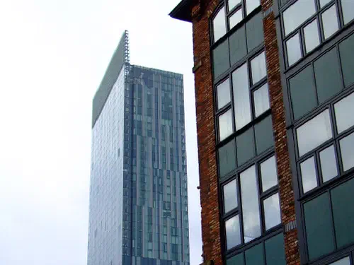 Tall blue glass skyscraper looms above a brick building against overcast gray sky.
