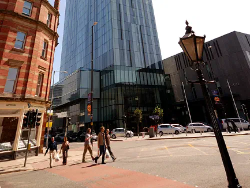 Low angle photo shows a tall modern building on a busy street corner under clear sky.