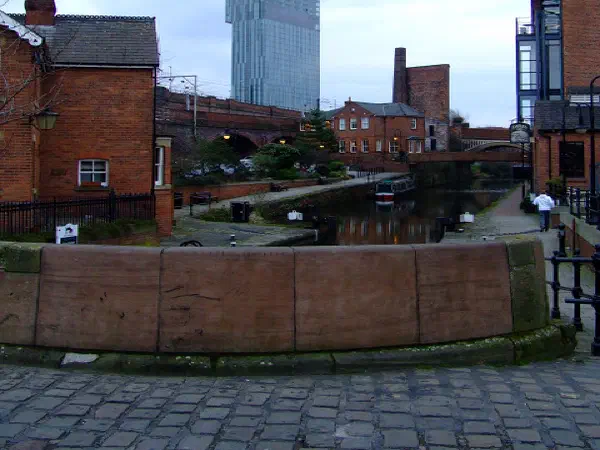 Brick structures line a canal under an overcast sky, contrasting with a modern glass skyscraper. — Beetham Tower, Manchester