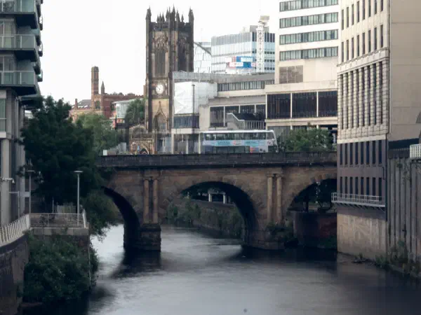 Stone arch bridge spans a calm waterway under modern and historic city buildings. — Blackfriars Bridge, Manchester