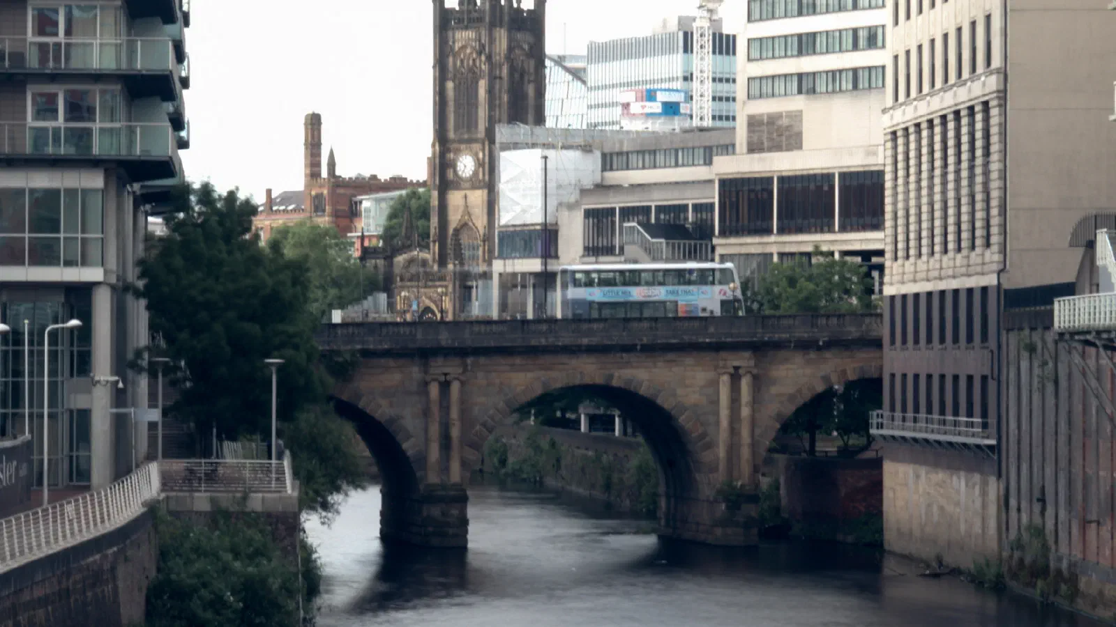 Stone arch bridge spans a calm waterway under modern and historic city buildings. — Blackfriars Bridge, Manchester