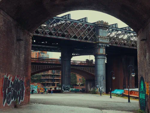 Graffiti-adorned brick archway frames industrial bridges over canal at dusk.