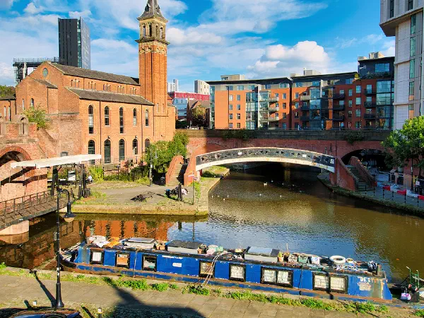 Blue narrowboat docked near arched bridges and brick buildings under bright sky. — Castlefield Canals, Manchester