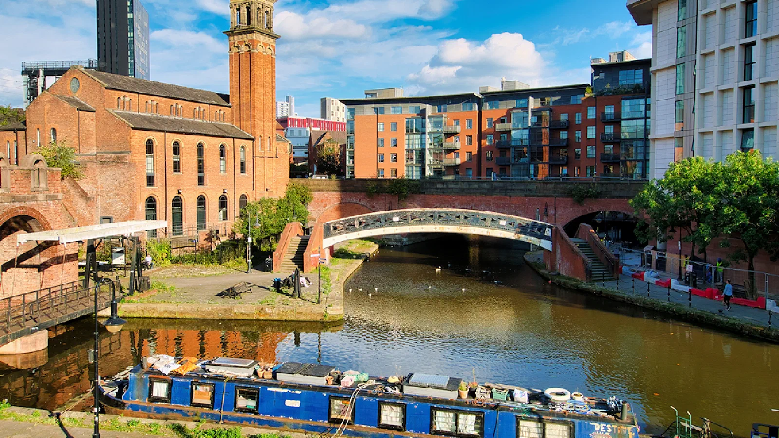 Blue narrowboat docked near arched bridges and brick buildings under bright sky. — Castlefield Canals, Manchester