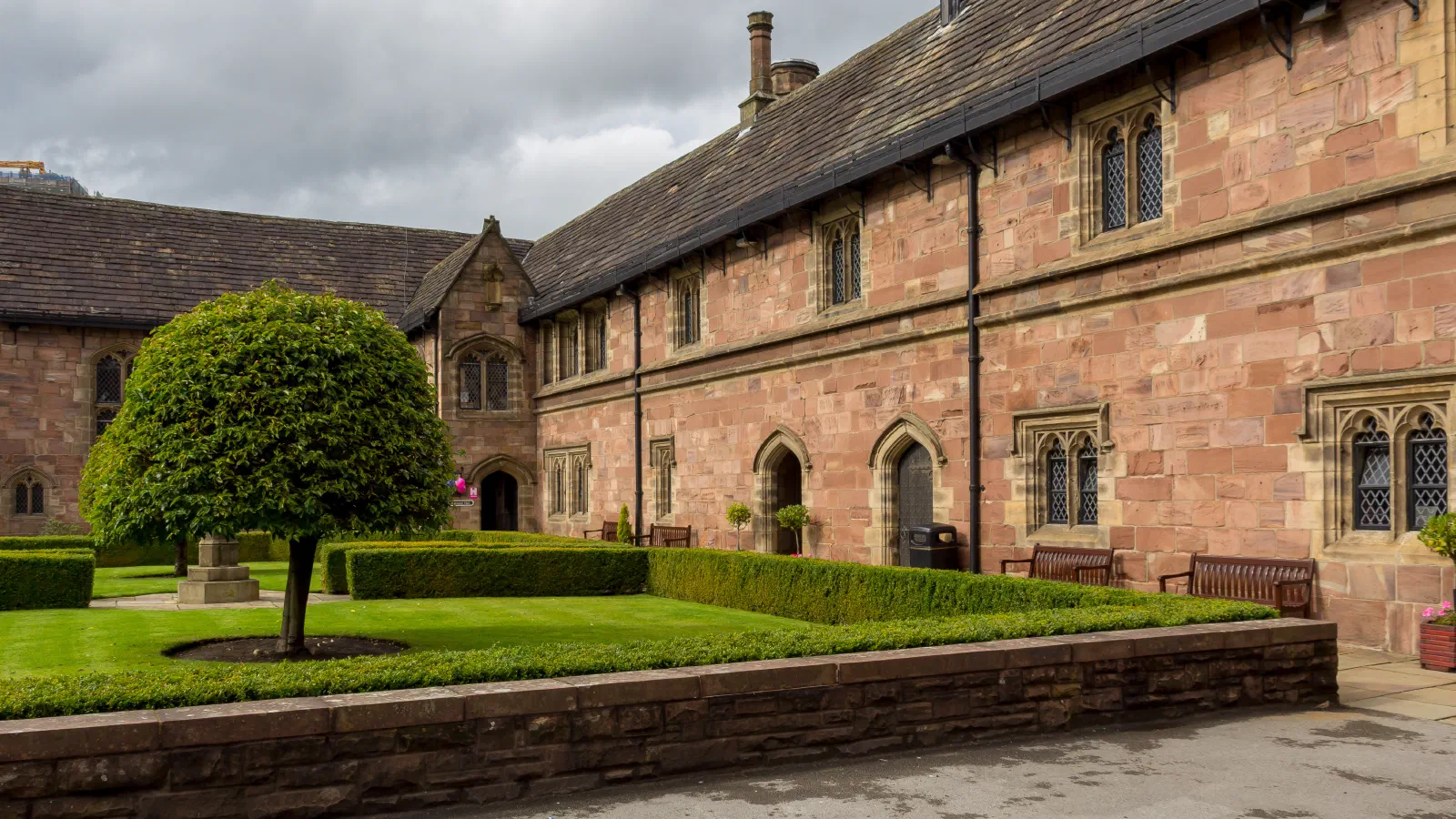 Stone building courtyard features well-manicured garden under cloudy sky. — Chetham’s Library, Manchester