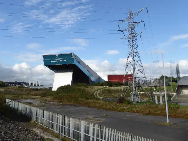 An overpass structure on a hillside near an electrical pylon under a blue sky. — Chill Factore, Manchester