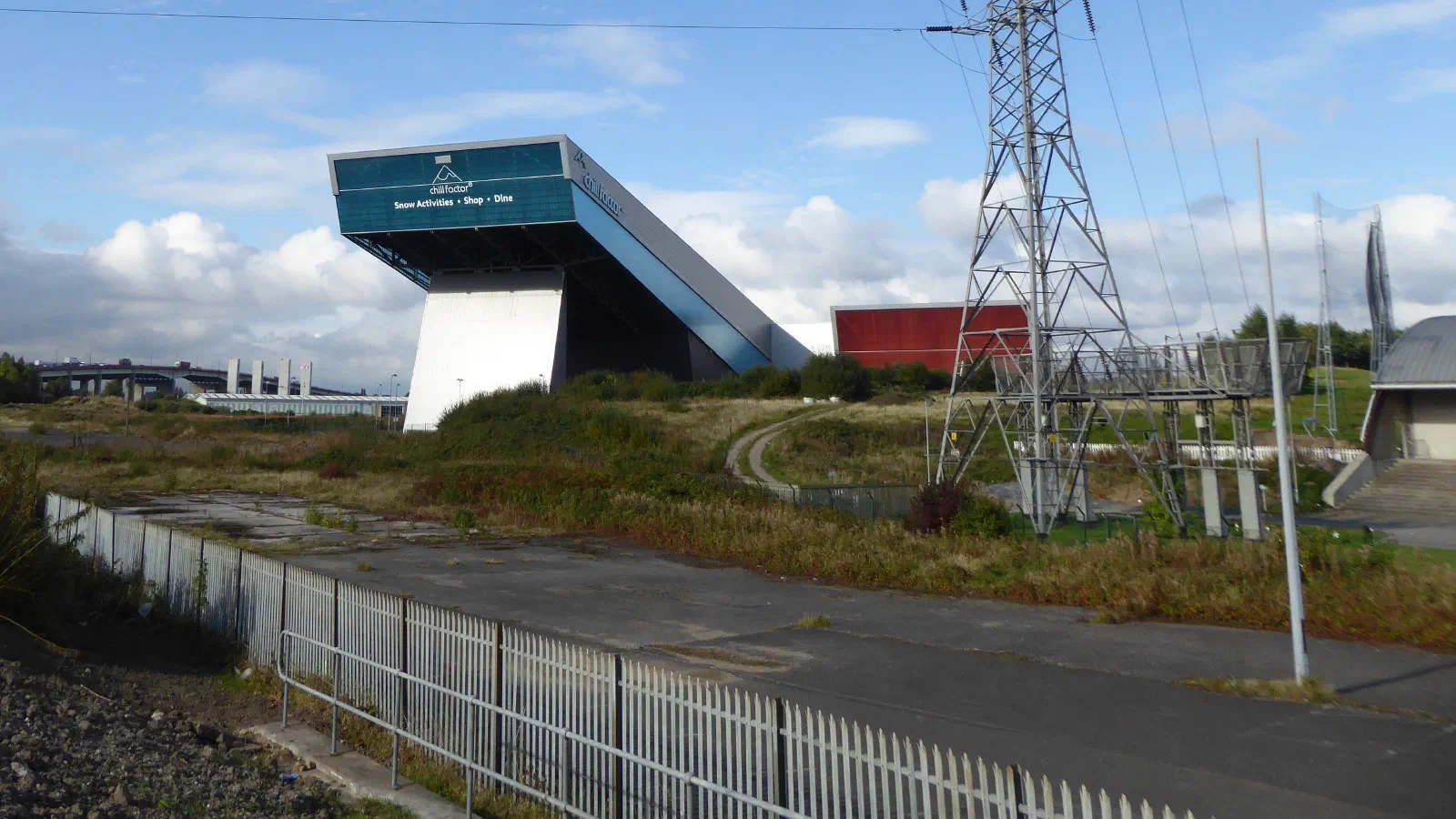 An overpass structure on a hillside near an electrical pylon under a blue sky. — Chill Factore, Manchester