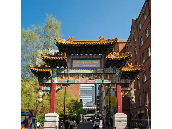 Colorful archway marks Chinatown entrance on sunny day with red-brick building to right. — Chinatown, Manchester