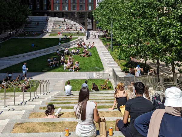 On a sunny day, people relax on steps between modern brick and beige buildings with green grass nearby. — Circle Square (Symphony Park), Manchester
