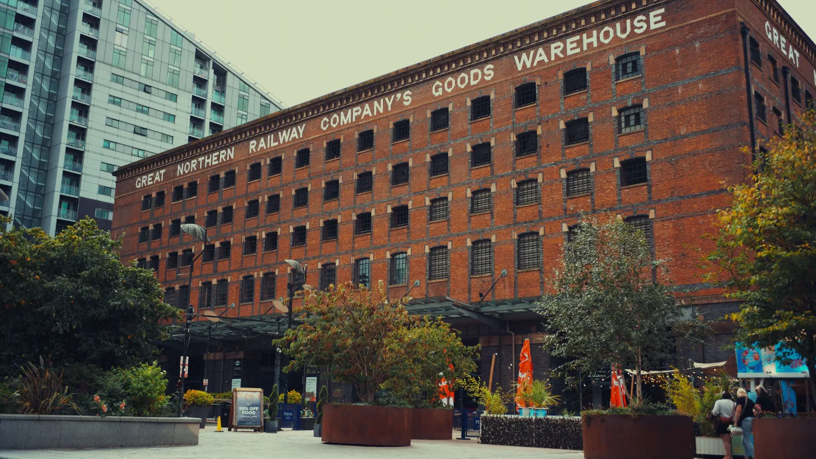 Red brick warehouse labeled Great Northern Railway Company's Goods Warehouse stands near trees and modern building. — Great Northern Warehouse, Manchester