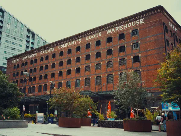 Red brick warehouse labeled Great Northern Railway Company's Goods Warehouse stands near trees and modern building. — Great Northern Warehouse, Manchester
