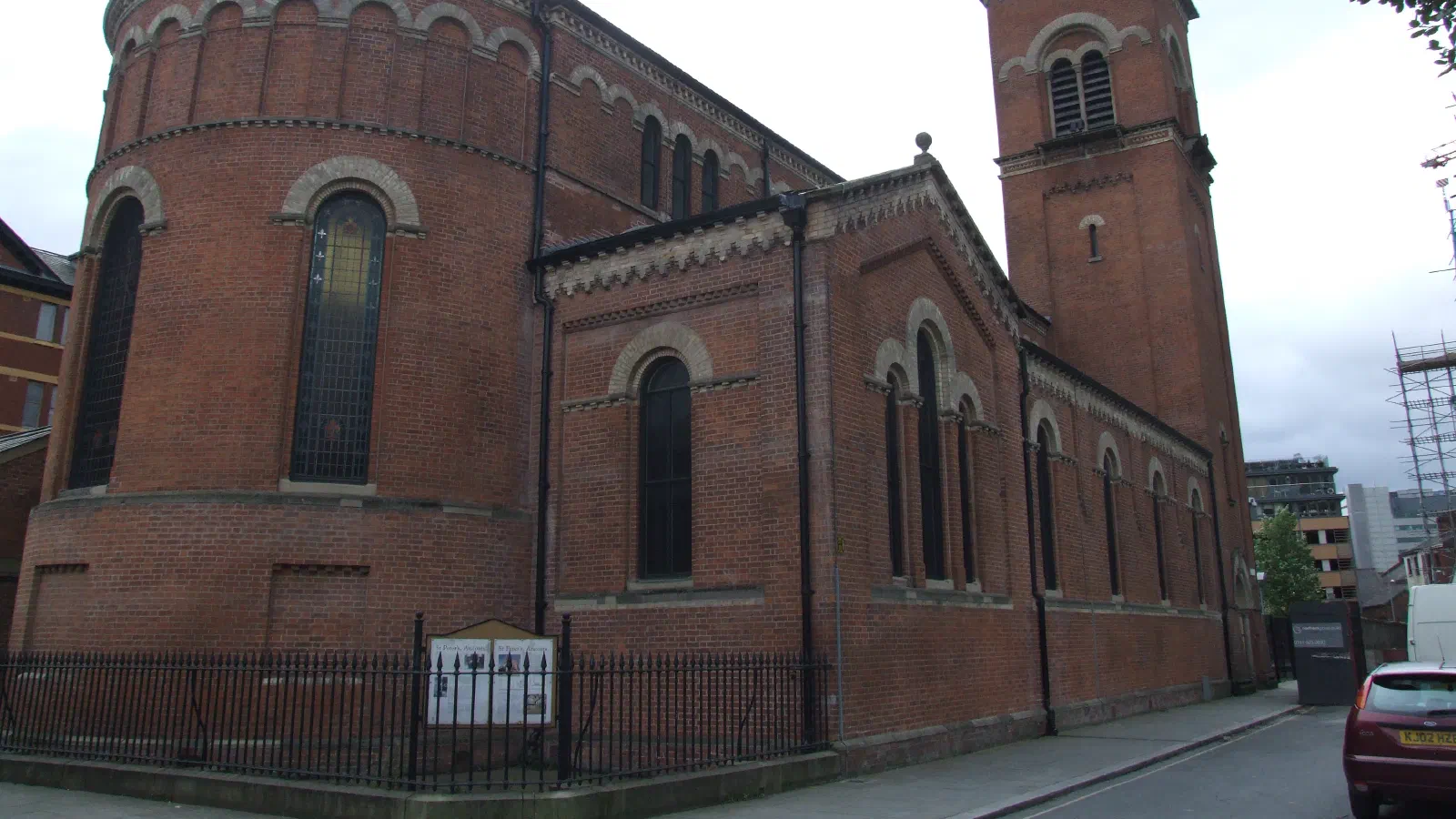 Red brick church with arched windows and bell tower surrounded by sidewalk under overcast sky. — Hallé St Peter's, Manchester