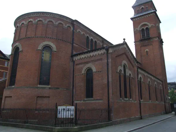 Red brick church with arched windows and bell tower surrounded by sidewalk under overcast sky. — Hallé St Peter's, Manchester