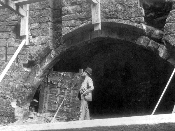Man stands inside arched stone building under wooden beams, observing a partially ruined brick wall interior. — The Hanging Bridge, Manchester