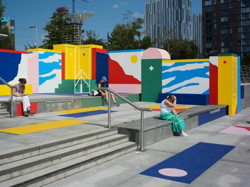 Colorful abstract murals on city stairs; three people relax under blue sky