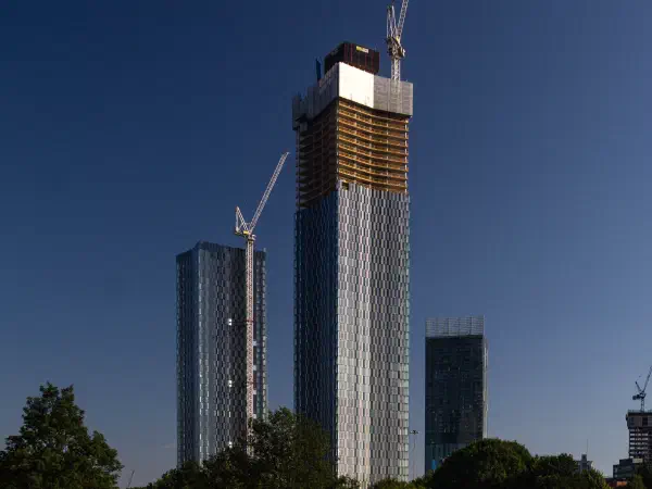 Two craned skyscrapers rise over grassy park against clear blue sky at midday sun. — New Jackson (Deansgate Square), Manchester
