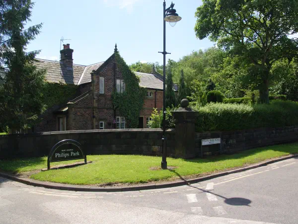 Sign for Philips Park by brick building and trees on sunny day. — Philips Park, Manchester