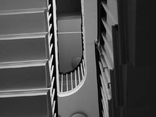 Black and white spiral staircase with visible balusters, steps and overhead light fixtures.