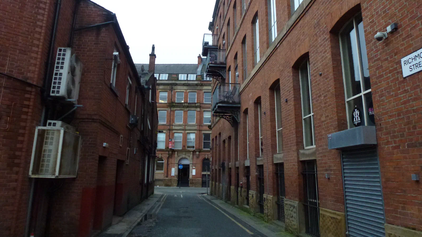 A narrow alley between brick buildings under an overcast sky, with visible street sign and air conditioning units. — Richmond Street, Manchester
