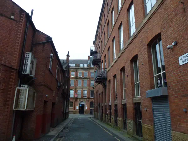 A narrow alley between brick buildings under an overcast sky, with visible street sign and air conditioning units. — Richmond Street, Manchester