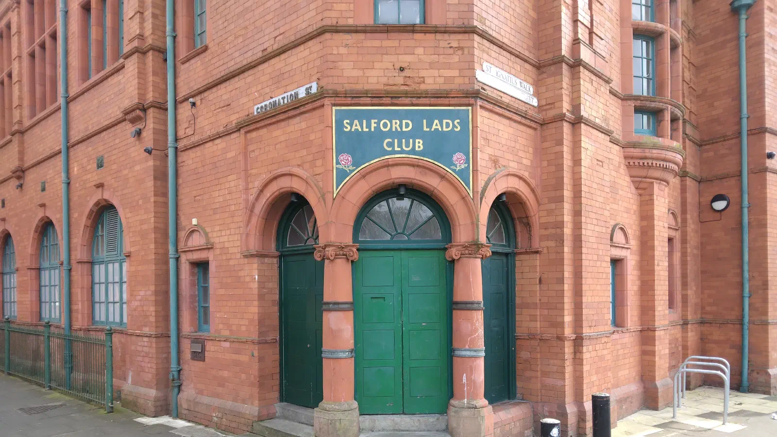 Red brick building entrance marked "Salford Lads Club" above green double doors under arches. — Salford Lads Club, Manchester