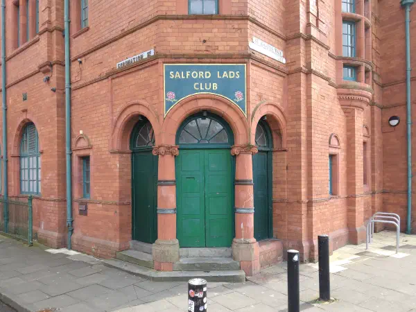 Red brick building entrance marked "Salford Lads Club" above green double doors under arches. — Salford Lads Club, Manchester