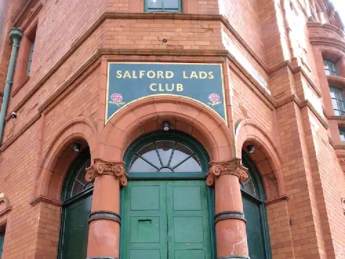Red brick building entrance with green doors and "Salford Lads Club" sign.