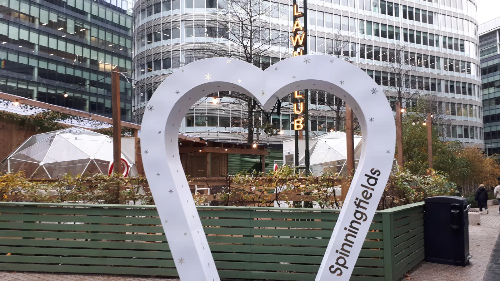 White heart sculpture with snowflake decorations stands outside a green fence on an urban street. — Spinningfields, Manchester