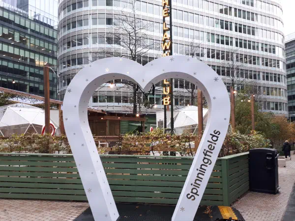 White heart sculpture with snowflake decorations stands outside a green fence on an urban street. — Spinningfields, Manchester