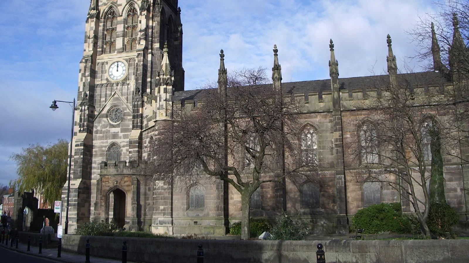 Stone church with clock tower, bare trees, blue sky. — St Mary’s Church & Staircase, Manchester