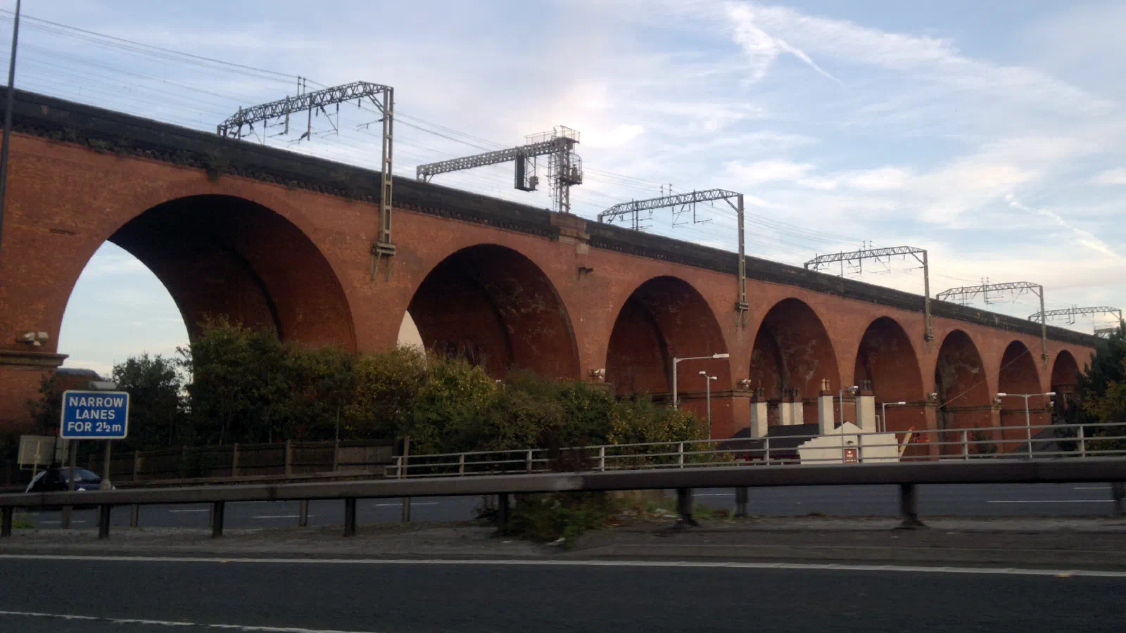 Tall red brick viaduct spans road under clear sky with overhead lines. — Stockport Viaduct, Manchester