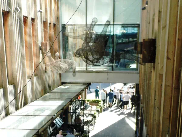 High-angle view of an open-air urban dining alley with sunlight casting shadows on walkways and seating areas. — The Avenue (Spinningfields), Manchester