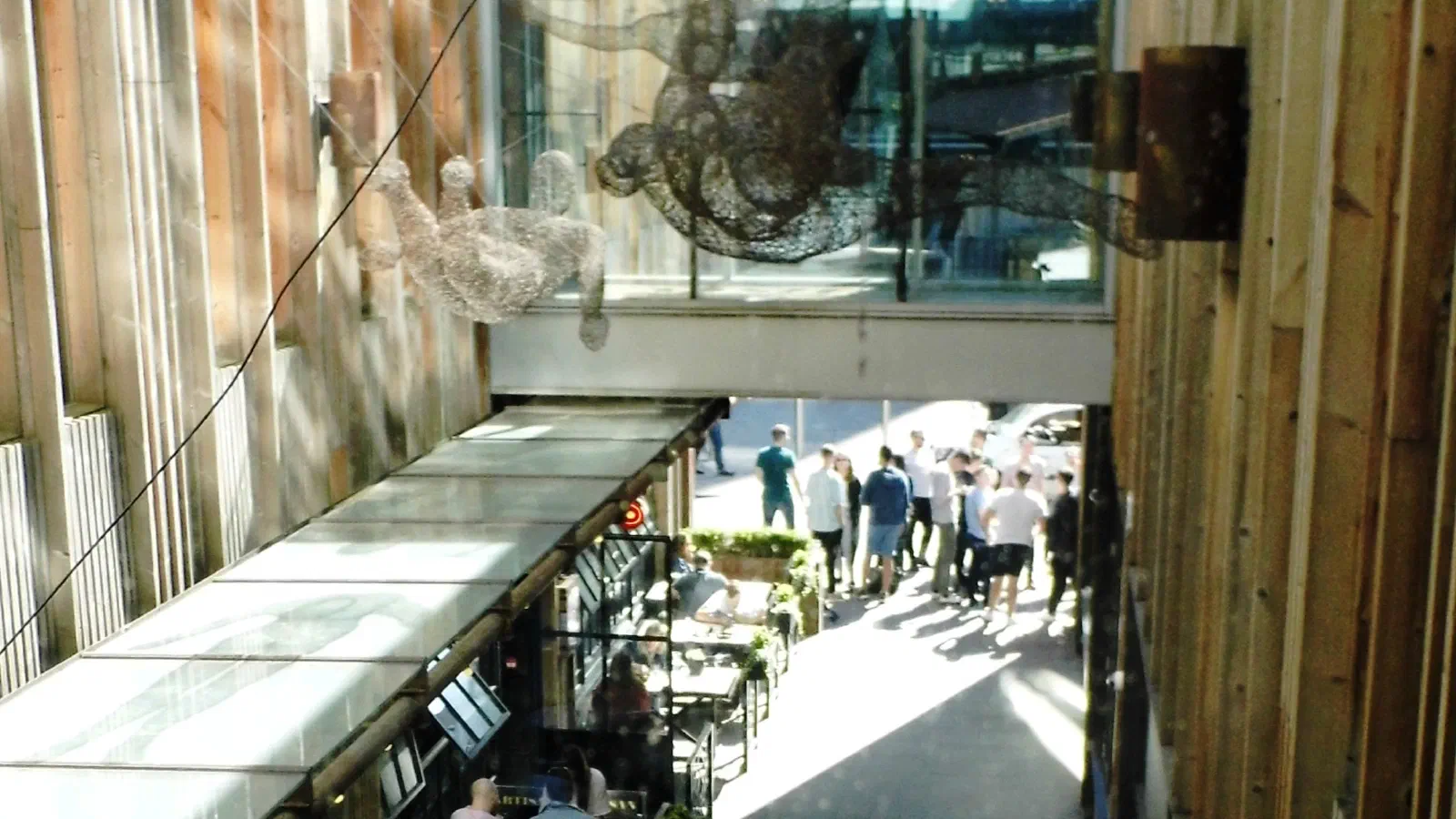 High-angle view of an open-air urban dining alley with sunlight casting shadows on walkways and seating areas. — The Avenue (Spinningfields), Manchester