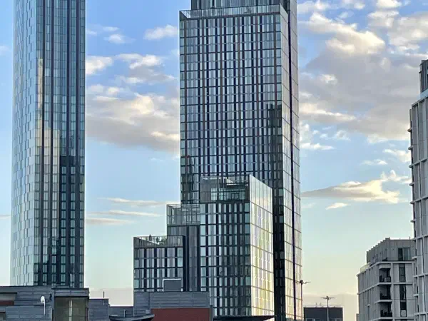 Modern glass skyscrapers rise against a blue sky with scattered clouds on an urban landscape. — The Blade & Three60, Manchester