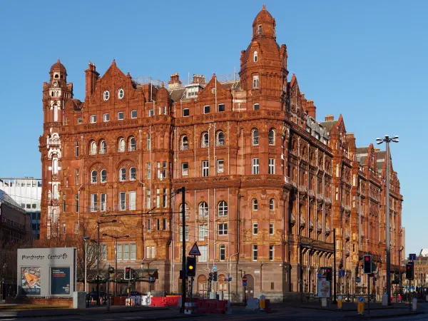 Sunlit red brick building with towers under a clear blue sky. — The Midland Hotel, Manchester