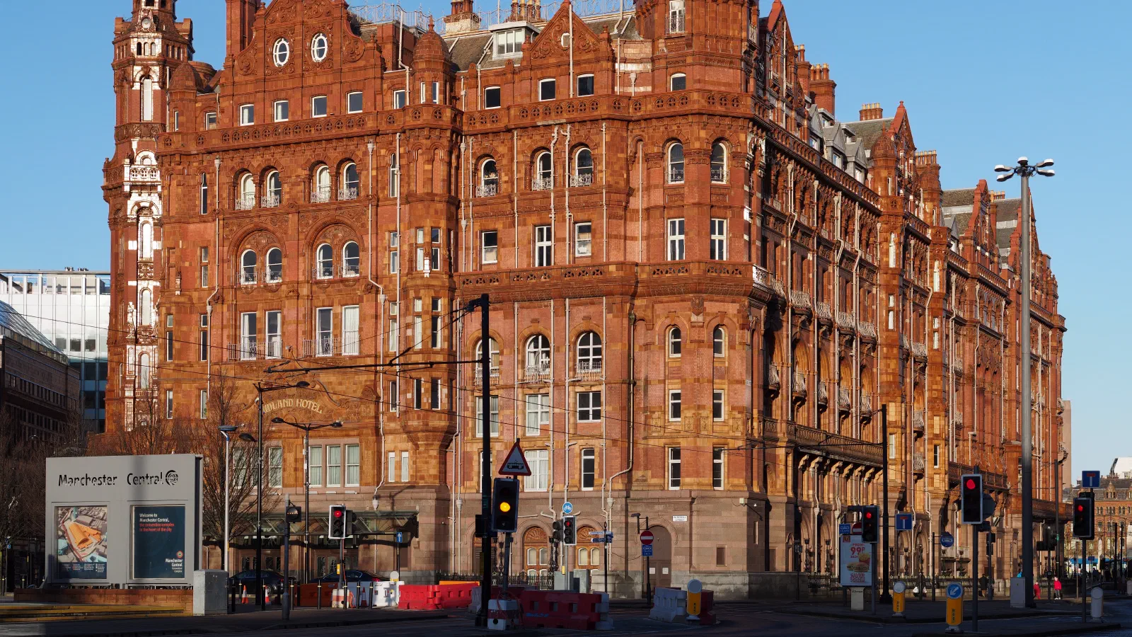 Sunlit red brick building with towers under a clear blue sky. — The Midland Hotel, Manchester
