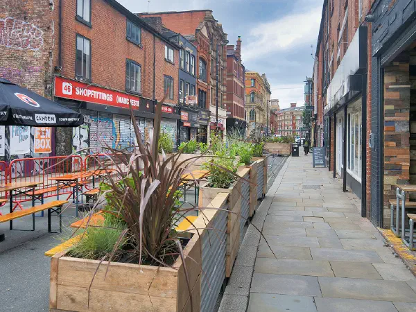 Outdoor seating lined with planters along a brick-paved street under cloudy skies. — Thomas Street, Manchester