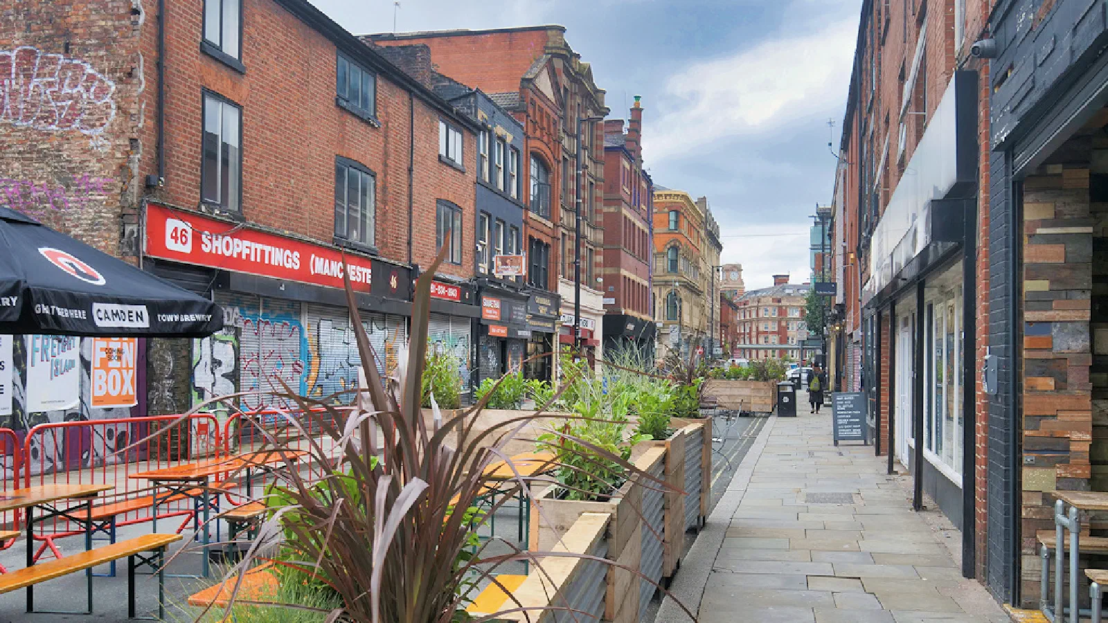 Outdoor seating lined with planters along a brick-paved street under cloudy skies. — Thomas Street, Manchester
