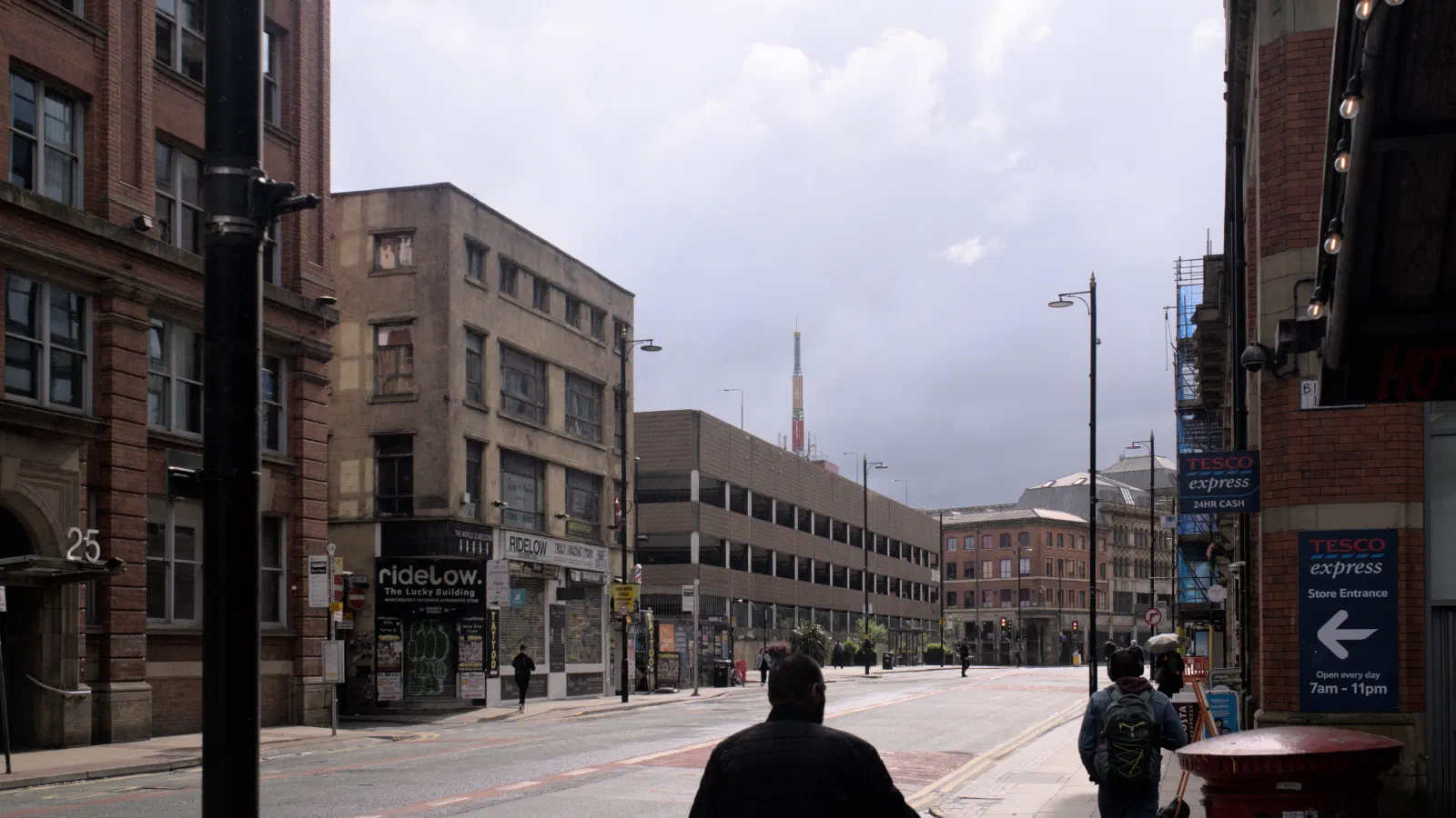 Street scene with brick buildings under overcast sky and pedestrians walking along sidewalk. — Tib Street, Manchester