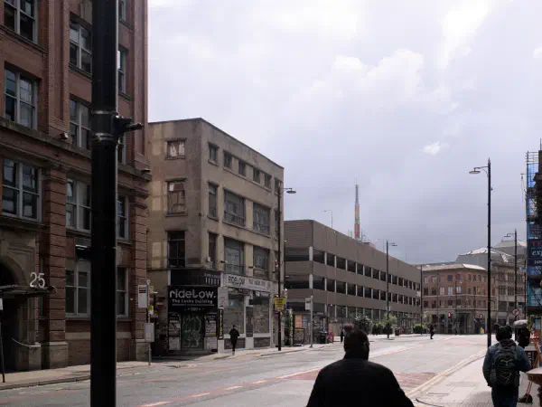 Street scene with brick buildings under overcast sky and pedestrians walking along sidewalk. — Tib Street, Manchester