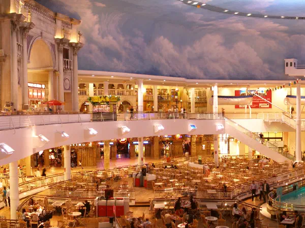 Wide-angle panorama shows a multi-level shopping mall's indoor atrium with restaurants and shops under a painted sky ceiling. — The Trafford Centre (The Orient), Manchester